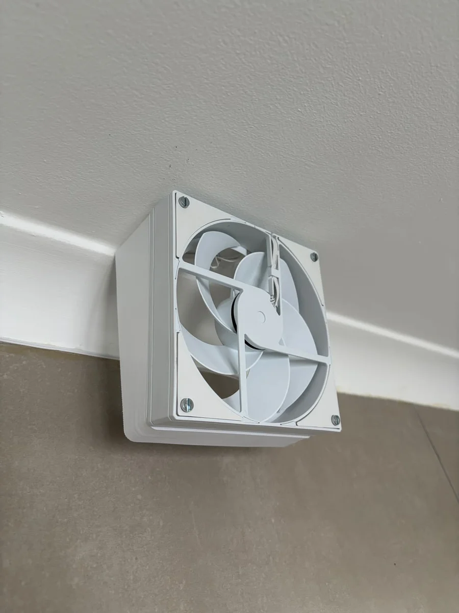 Close-up of the 3D printed fan riser mounted in the bathroom vent, showing the case fan through the grille